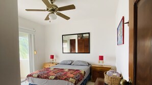 Ein Schlafzimmer mit einem Bett, Deckenventilator, Nachttisch und Spiegel.