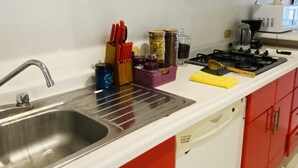 Eine Küche mit roten Schränken, einer Edelstahl-Spüle sowie verschiedenen Küchengeräten und Utensilien.