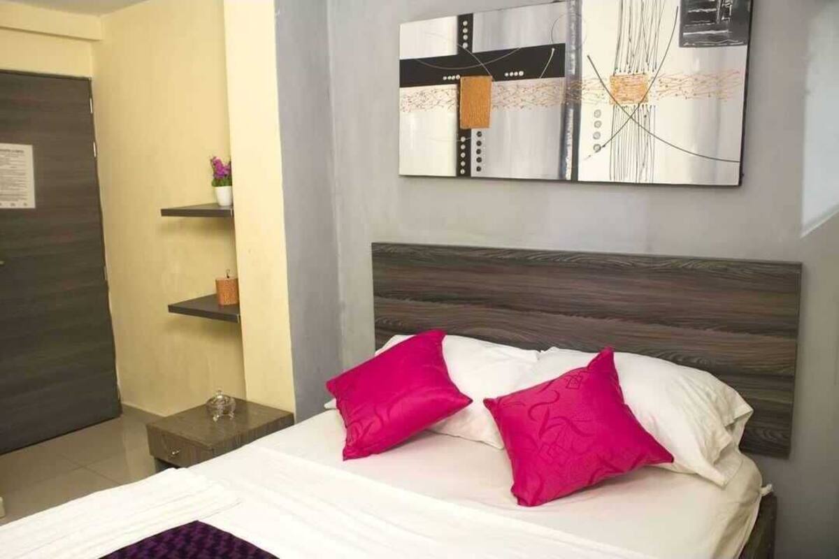 Ein Hotelzimmer mit Bett, zwei Kissen, einem Nachttisch, einem Spiegel und einer Wand mit abstrakter Kunst.