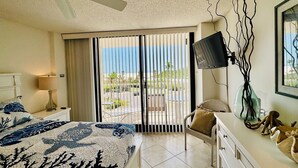 Habitación de hotel con cama, televisor, silla, cómoda y vistas al exterior.