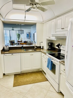 A modern kitchen with white cabinetry, a granite countertop, a built-in oven, and a ceiling fan.