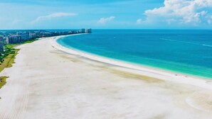 Une vaste plage bordée par un océan d’un bleu limpide, avec une vue sur la ville en arrière-plan.