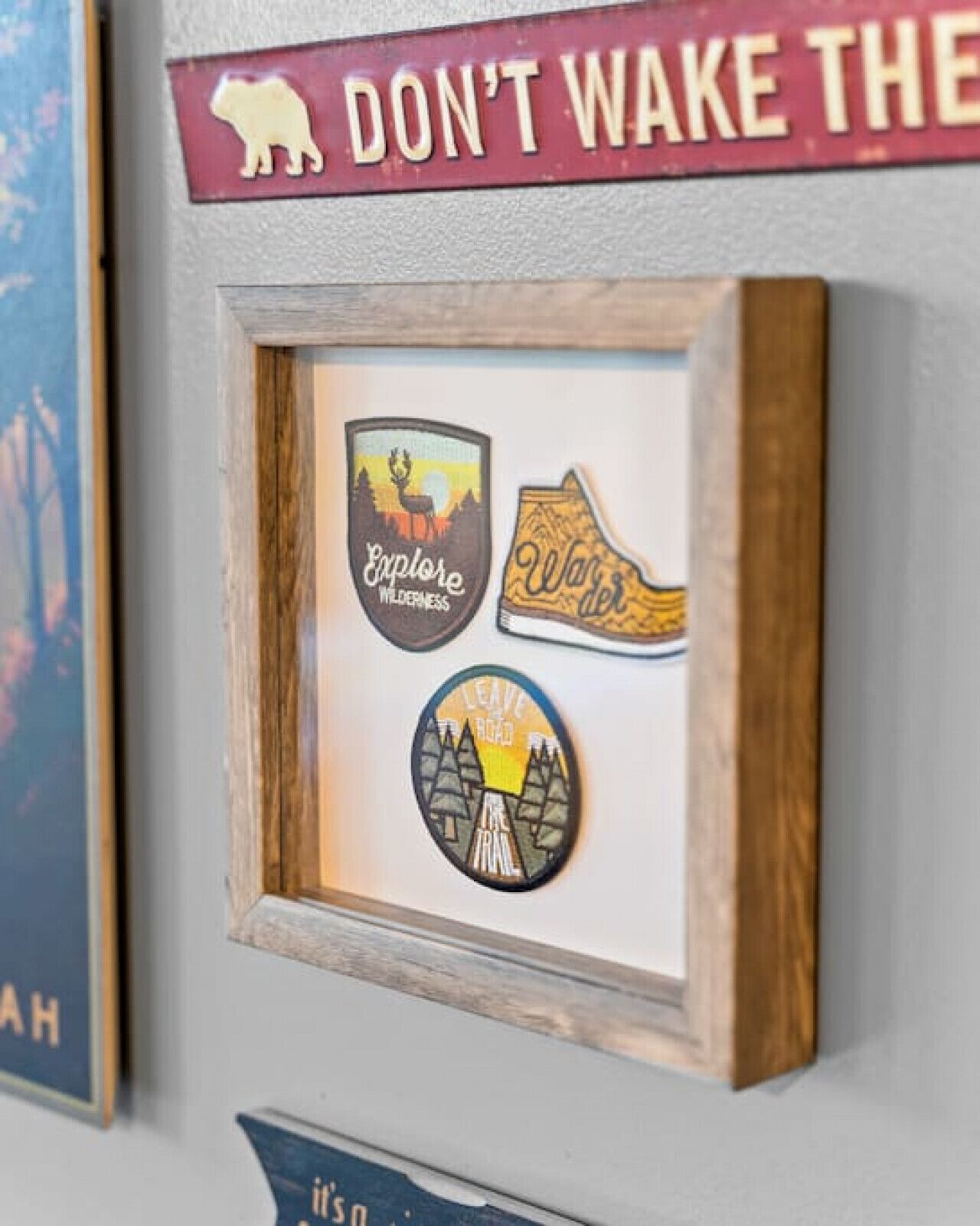 Uma parede com um quadro de um urso, uma placa que diz "NÃO ACORDA O URSO", e três adesivos: um com um veado, um com um urso e um com uma paisagem de montanha.