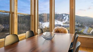 Een eetruimte met een houten tafel en stoelen, grote ramen met uitzicht op een besneeerd landschap en een waterval.