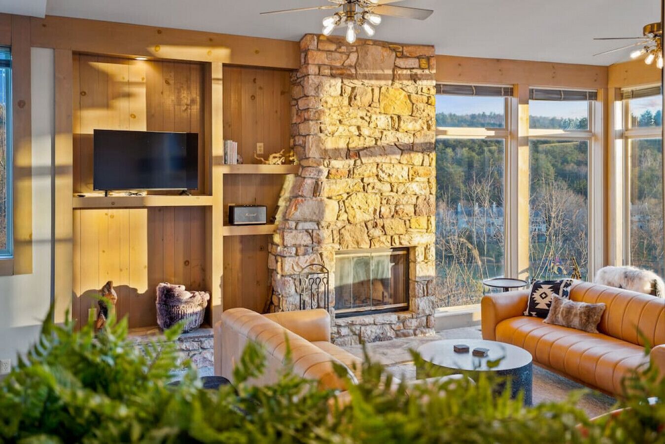 A modern living room with a stone fireplace, leather sofa, and a flat-screen TV mounted on the wall.