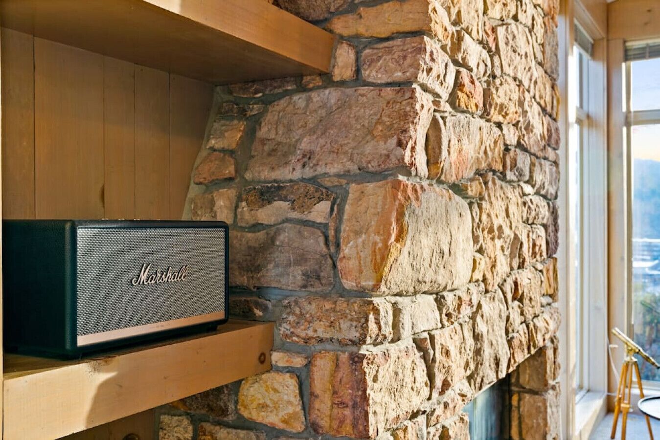 A Marshall speaker on a wooden shelf against a stone wall.