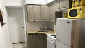 A compact kitchen with grey cabinets, a white refrigerator, a stove, and a yellow microwave.