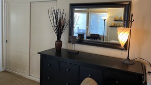 A room with a black dresser, a mirror, a vase with branches, and a lamp. - Charming Studio w/ Fireplace & Kitchen — Steps to Sand (Manhattan Beach)