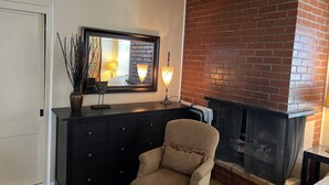 A living room with a fireplace, a dark wooden dresser, a chair, and a large mirror reflecting the room. - Charming Studio w/ Fireplace & Kitchen — Steps to Sand (Manhattan Beach)