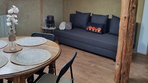 Un espai vital estilitzat en estudi amb menjador que destaca per una taula i cadires de fusta, un sofà amb coixins, i un gran biga de fusta.
