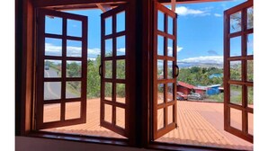 Vista a través de ventanas de madera abiertas con techo de lámina corrugada, mostrando una carretera y edificios.