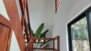 Una escalera de madera con barandilla, un ventilador de techo y un ventanal con vistas al follaje exterior.