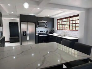 A modern kitchen with a marble countertop, stainless steel appliances, and a large window with a grid pattern.