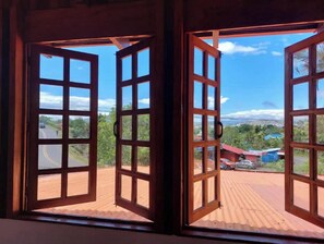 A view through open wooden-framed windows with a corrugated metal roof, overlooking a road and buildings.