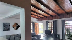 Una sala de estar moderna con techo de madera, un conjunto de sofás, una mesa de comedor y un amplio ventanal con cortinas.