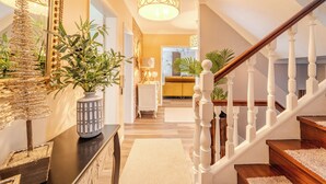 A staircase with white balusters leading to a second floor. A decorative lamp hangs above the staircase, and a vase with green plants is on the landing.