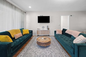 A living room with two green sofas, a round wooden coffee table, and a patterned rug.