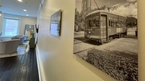 A hallway with a vintage tram poster, a modern sofa, and a window with blinds. - Limited Offer: Cozy Condo by French Quarter (New Orleans)