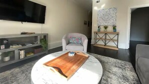 A modern living room with a flat-screen TV, a round coffee table, a grey sofa, and a console table with decorative items. - Limited Offer: Cozy Condo by French Quarter (New Orleans)