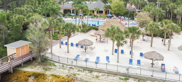 A resort with a pool, lounge chairs, palm trees, and a beach area.