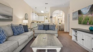 Una sala de estar con dos sofás grises, una mesa de centro, una zona de comedor con mesa y sillas, y una cocina al fondo.