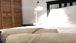 Un letto rifatto con una coperta bianca e cuscini, una lampada da comodino e un armadio in legno.