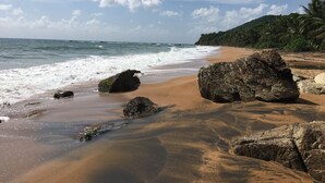 Una spiaggia con rocce grandi, acqua cristallina e una collina lontana ricoperta di vegetazione.