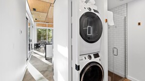 Lavanderia moderna con una lavatrice a carica frontale di grandi dimensioni, un box doccia in vetro e vista sull'esterno attraverso un'ampia finestra.