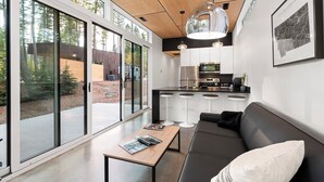 A modern kitchen with a central island, a dining area with a sofa and table, and large windows offering a view of the outdoors. - The Clark Fork at Stoner Creek Cabins (Lakeside)