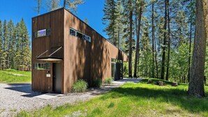 A modern wooden cabin with large windows, surrounded by a forest. - The Bitterroot at Stoner Creek Cabins (Lakeside)