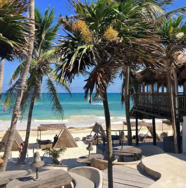 Relax on the beachfront deck with comfortable seating and a thatched-roof structure nearby.