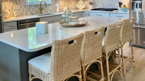 Una cocina moderna con armarios blancos, una isla grande con taburetes de mimbre e iluminación colgante.