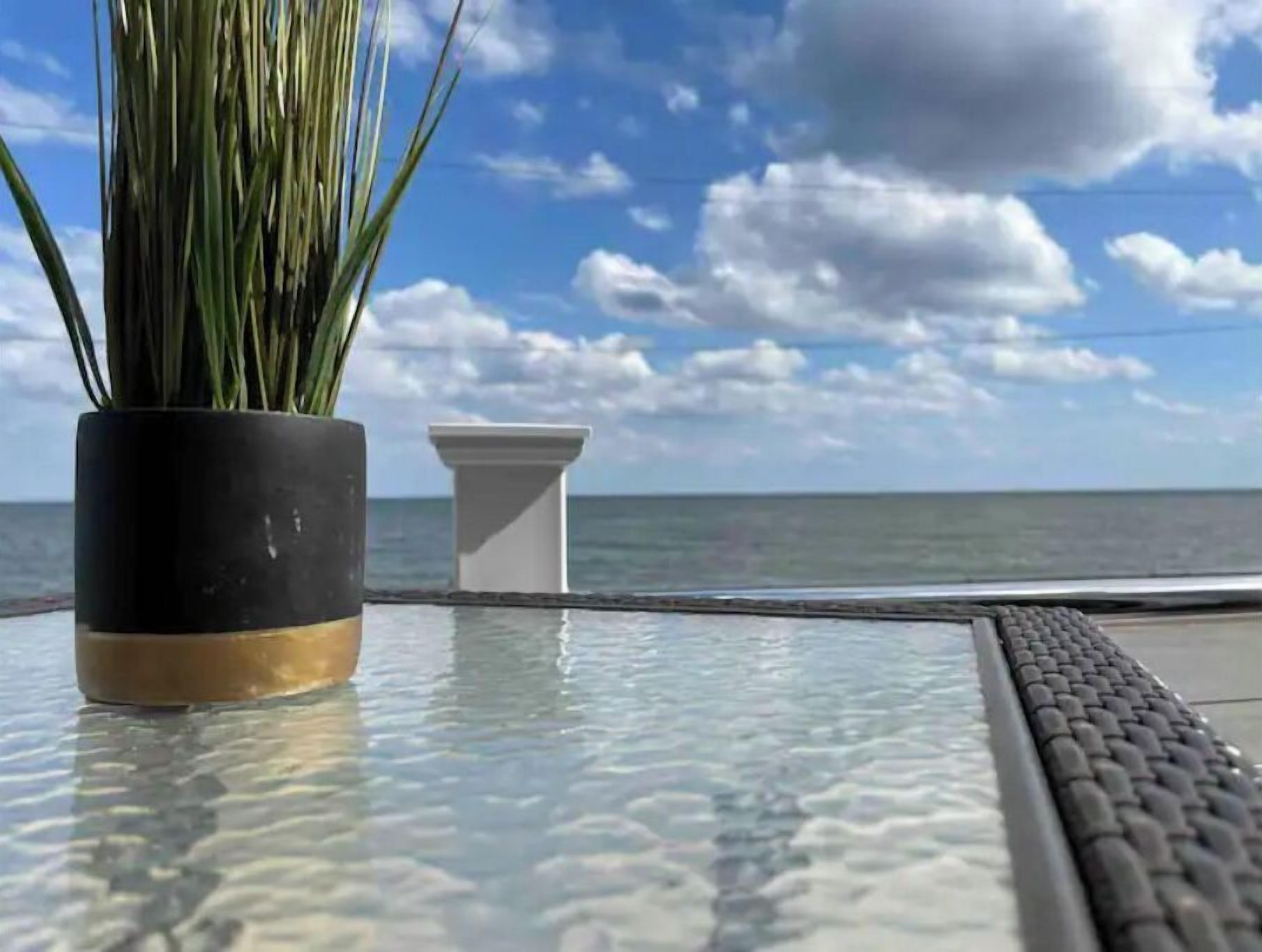 A glass table with a potted plant and a white vase by the sea.
