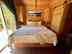 Un dormitorio de cabaña de madera con una cama, dos mesitas de noche, un cuadro colgado y una puerta corredera.