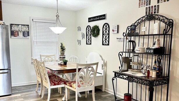 A dining area with a wooden table and chairs, a hanging light fixture, and a metal rack with kitchen items. - 🏡 Cozy Home <5 Miles to Boat Ramp—Book Now! (Scottsboro)