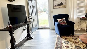 A living room with a flat-screen TV, a dark wooden coffee table, a blue armchair with a decorative pillow, a patterned rug, and a door leading outside. - 🏡 Cozy Home <5 Miles to Boat Ramp—Book Now! (Scottsboro)