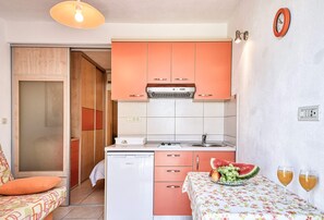 A compact kitchen with pink cabinets, a white countertop, and a sink. There is a fruit bowl on the counter and two glasses of orange juice. - Apartments Gracin - One Bedroom Apartment with Terrace (Povlja)