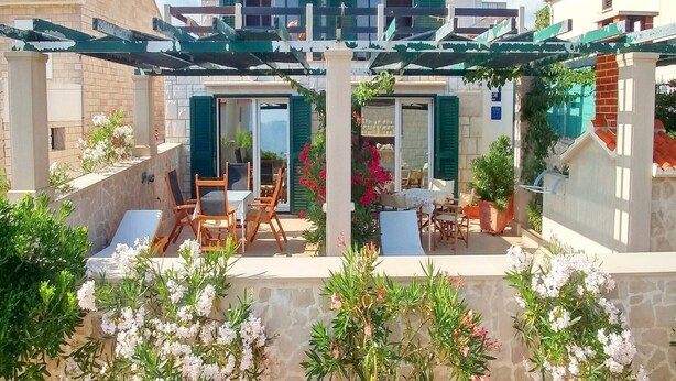 A two-story house with a patio area featuring outdoor furniture and potted plants.