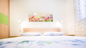 A hotel room with a bed, two pillows, a headboard, and a wall-mounted picture of flowers.