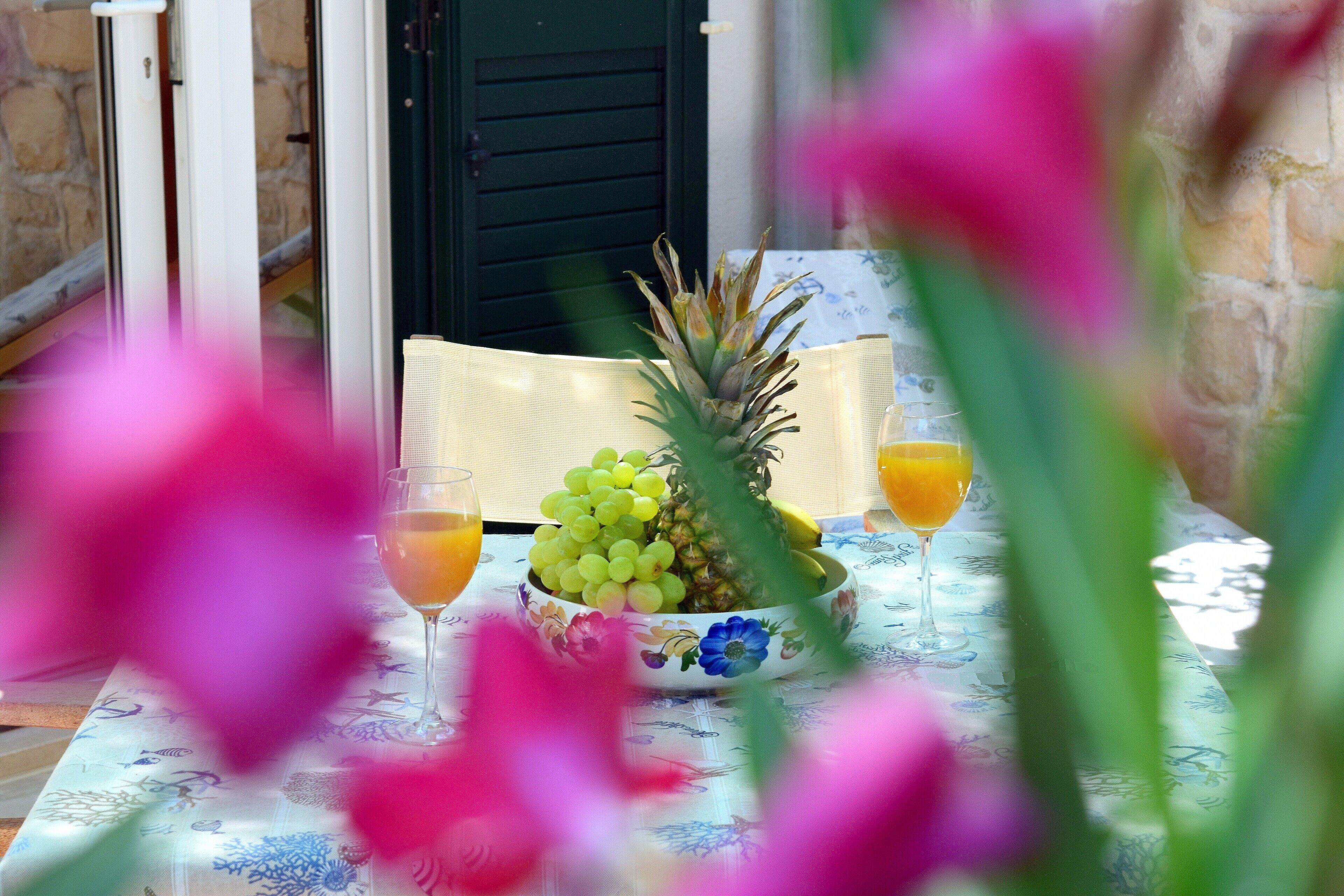 A table with a floral tablecloth, a bowl of fruit, and two glasses of orange juice.