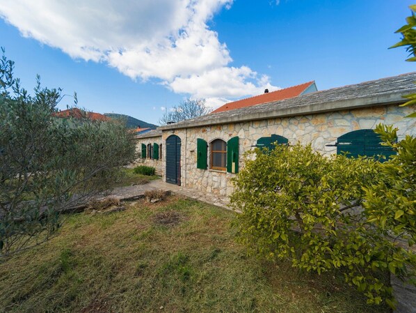 A stone building with green shutters, a stone pathway, and surrounding greenery.