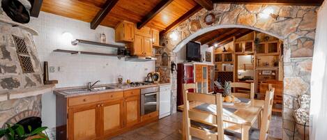 A rustic kitchen with wooden cabinets, a stone archway, and a dining area with wooden chairs.