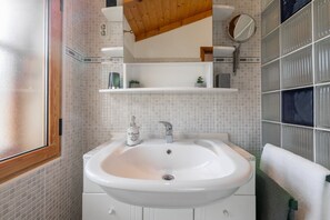 A bathroom with a white sink, a mirror, and a window with a wooden frame.