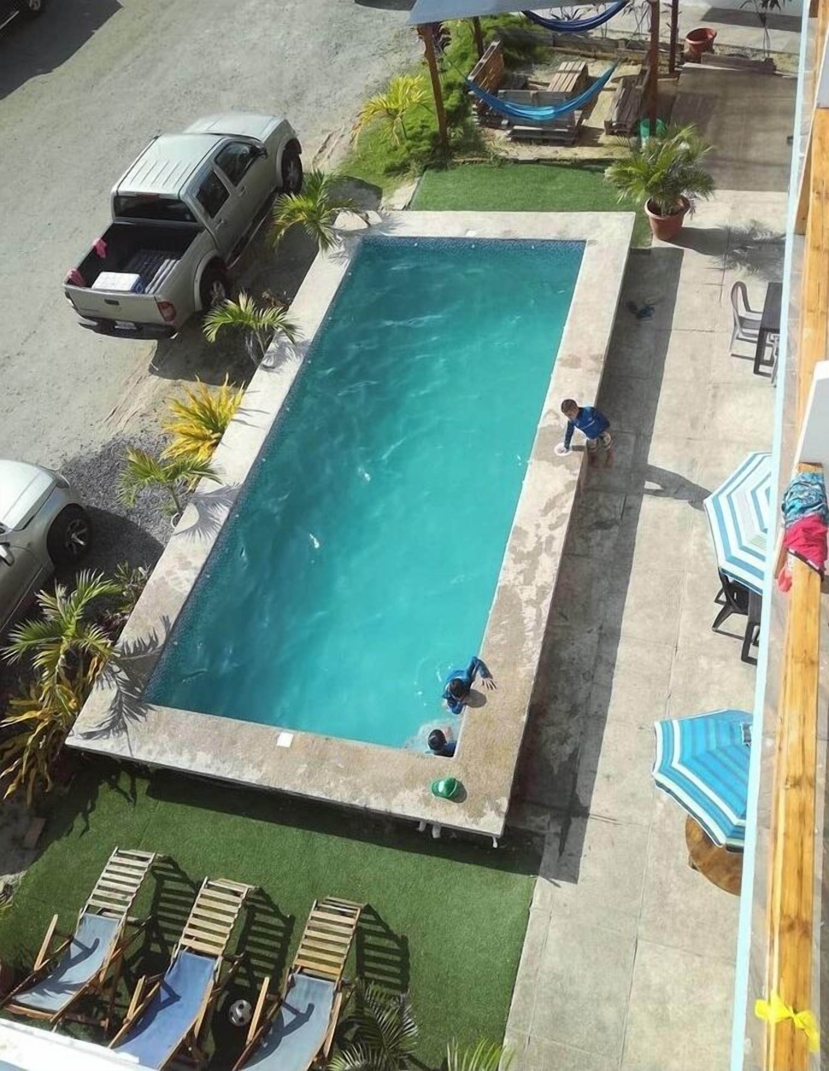 Una piscina rectangular con borde de hormigón, rodeada por un patio con sillas de descanso y una hamaca.