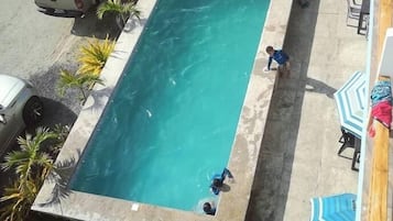 Una piscina rectangular con borde de hormigón, rodeada por un patio con sillas de descanso y una hamaca.