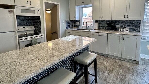 A modern kitchen with white cabinets, a granite countertop, a built-in oven, and a coffee maker. - Charming Football Hall of Fame Bungalow (Canton)
