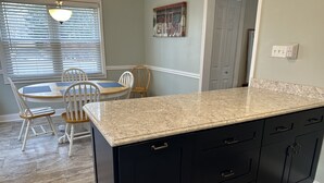 A kitchen with a granite countertop, black cabinets, and a dining area with a table and chairs. - Charming Football Hall of Fame Bungalow (Canton)