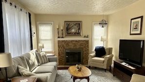 A living room with a sofa, armchair, coffee table, fireplace, television, and decorative items. - Charming Football Hall of Fame Bungalow (Canton)