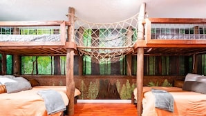 A room with two bunk beds, a hammock, and a forest mural on the wall.