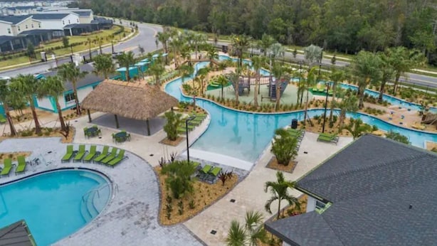 Ein Resort mit großzügigem Poolbereich, mehreren Liegestühlen und einer Struktur mit Reetdach.